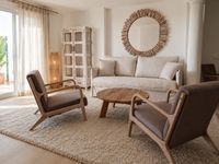 Relaxed family living room in Bendinat Golf with natural linen sofa, wooden lounge chairs, soft wool rug and calm Mediterranean
