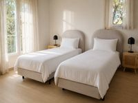 Bright twin bedroom in Bendinat Golf with upholstered headboards, white cotton bedding, linen curtains and calm Mediterranean styling on Mallorca.